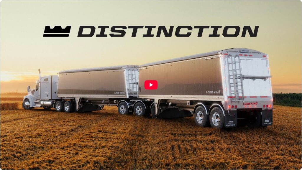 A silver semi-truck with two large trailers drives through a field at sunset, with the word "DISTINCTION" and a crown-like logo above.